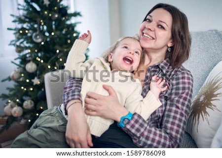Cute little kid playing with mum in the room. Christmas tree with lights on a background