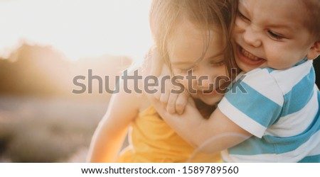 Close up portrait of a lovely little kid embracing with love his sister against sunset.