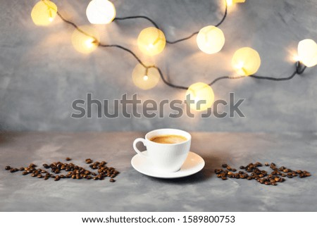 Christmas picture with cup of coffee surrounded by fir branches on gray table.