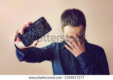 Bearded upset man holds a out-of-use tablet or smartphone. on a light background. Broken screen