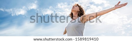 mindfulness - zen yoga woman opening up her chakra with arms raised,practicing meditation for freedom over summer blue sky,low angle view, long banner Royalty-Free Stock Photo #1589819410