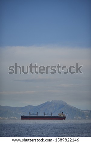 A vertical picture of a ship on a sea with mountains on the background under a cloudy sky