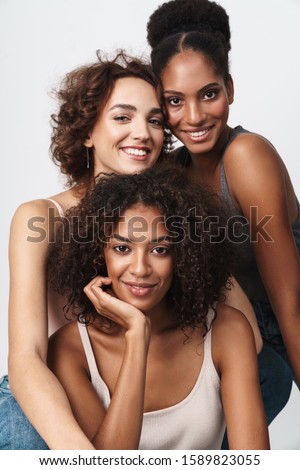Portrait of three beautiful multiethnic women standing together and smiling at camera isolated over white background Royalty-Free Stock Photo #1589823055