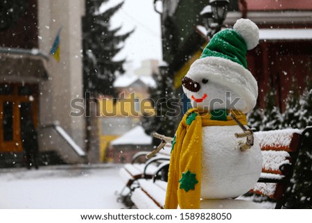 snowman in the forest in Christmas clothes, next to the tree