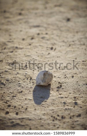A vertical picture of stone with its reflection on the ground surrounded by dust and sand