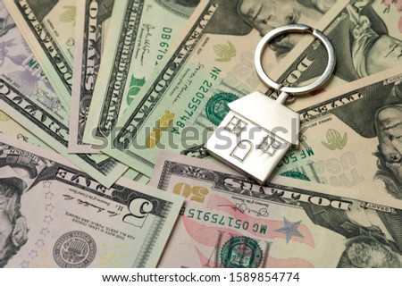 Close-up keychain in the house shape and lies on paper dollar bills. Mortgage concept repair styles on credit. Affordable housing and financial repair costs