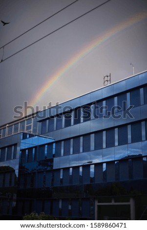 A modern blue building with a rainbow on the background under a blue sky in the evening