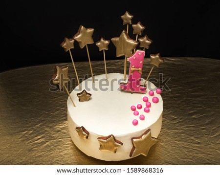 Birthday cake decorated with pink number 1 and gold stars of gingerbread on a dark background