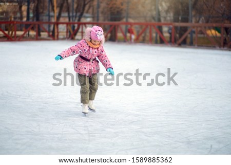 Girl uncertainly stands on figure skates on an ice rink and tries to ride.