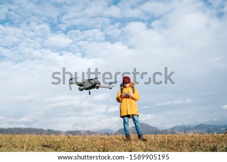 Teenager boy dressed yellow jacket piloting a modern digital drone using remote controller