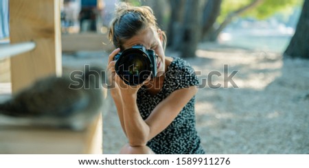 Young female photographer taking photo of a dove bird sitting on porch in summer resort.