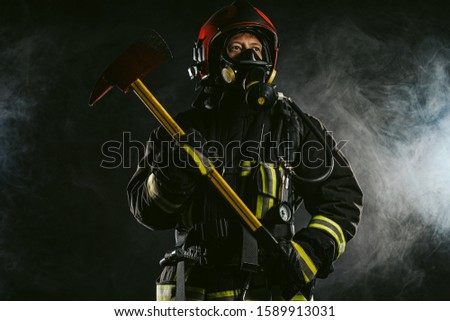portrait of professional and confident fireman holding hammer, wearing protective uniform and helmet on head, stand isolated in smoky background