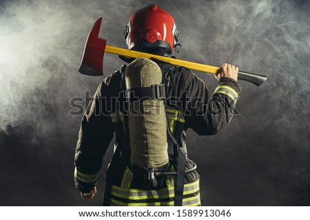 rear view on extinguisher stand holding hammer isolated over smoky background, wearing red helmet and uniform
