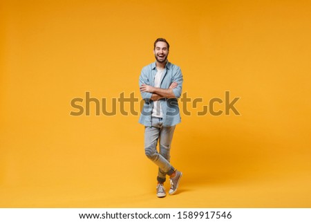 Laughing young bearded man in casual blue shirt posing isolated on yellow orange wall background, studio portrait. People sincere emotions lifestyle concept. Mock up copy space. Holding hands crossed Royalty-Free Stock Photo #1589917546