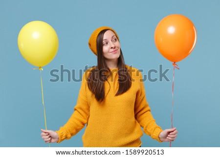 Pretty young woman girl in sweater hat posing isolated on blue background studio portrait. Birthday holiday party, people emotions concept. Mock up copy space. Celebrating hold colorful air balloons