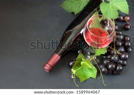 red wine in glasses, bottle of wine and grapes and grapes green leaves on black background, flat lay, view of top	