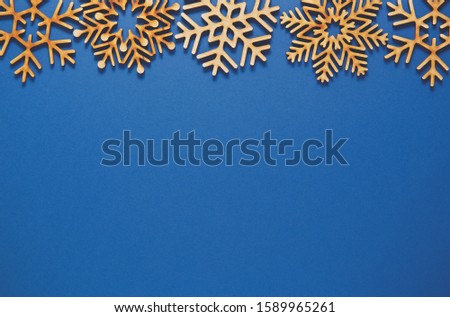 Flat lay Christmas background.Blue poster template with empty space for text.Winter holiday wallpaper with handmade wooden snowflakes.New Year celebration postcard in rustic design