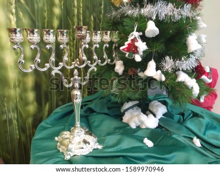Chanukah and Christmas symbols
Silver Hanukkah menorah
And fir tree decorated for the holiday 
Set on a bottle of green bottle, and a wall with a blurred green wheat wallpaper in the background
