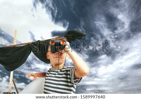 Little child boy playing with cardboard ship on blue wall background