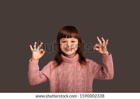 Funny joyful child girl shows a cute gesture two hands up, in a playful way, says that she has everything super and shows OK with both hands