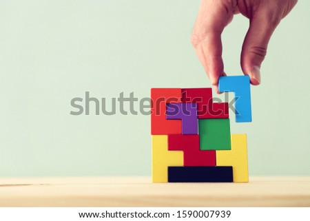 man's hand holding a square tangram puzzle, over wooden table
