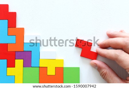 man's hand holding a square tangram puzzle, over wooden table