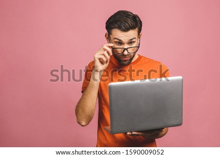 Confident business expert. Confident young amazed handsome man in casual holding laptop and smiling while standing against pink background.