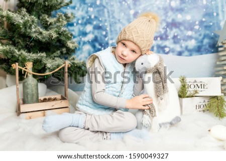 Little boy sitting with soft toy penguin on winter decorated background