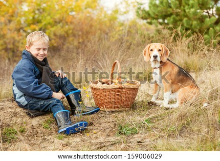 Little boy with his pet sit on clearing in the woods with basket full of mushrooms