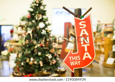 A closeup shot of a red arrow Santa this way signage with the decorated Christmas tree in the background