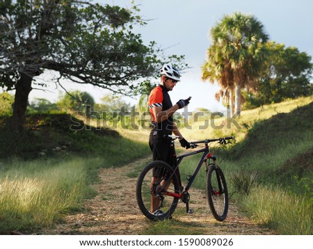 People, sports, active lifestyle and modern technology. Outdoor picture of cyclist on mountain bike using navigator on smart phone, exploring map and searching GPS coordinates while biking.
