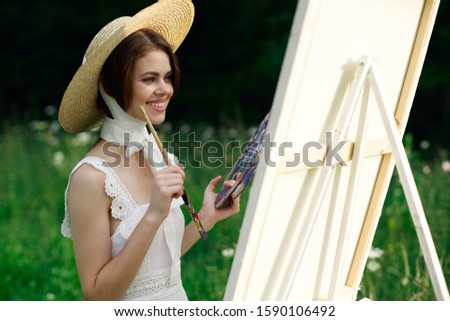 young woman paints a picture on a white canvas with paints and a brush