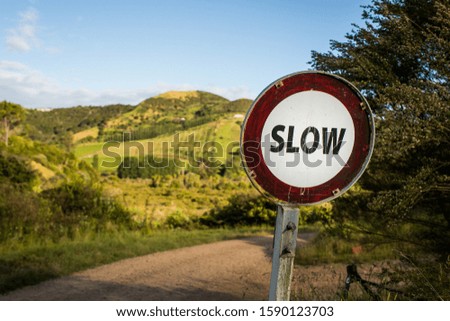 A Slow street sign with the greenery and high mountains i the background