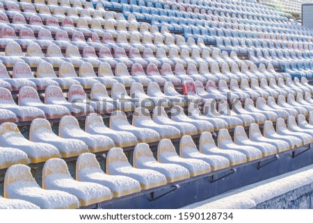 Stadium seats in the snow in winter. Snow-covered multi-colored seats at the stadium in winter. Snowfall interferes with sports. Uncleaned stadium.