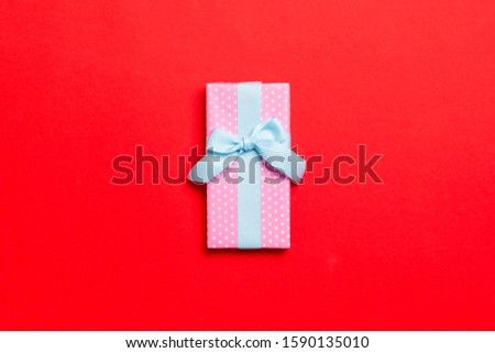 wrapped Christmas or other holiday handmade present in paper with blue ribbon on red background. Present box, decoration of gift on colored table, top view with copy space.
