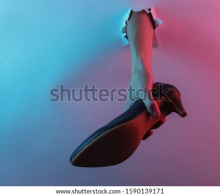 Hand holding high heel shoes through torn hole. Creative pop art pink blue neon color. Trendy gradient illumination. Night light