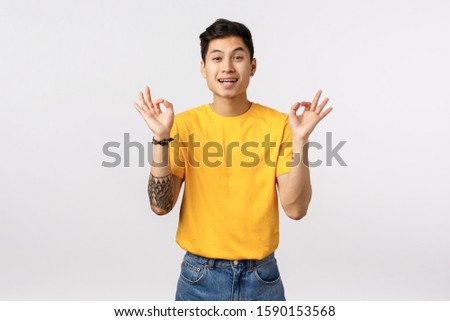 Guy trying calm down friend, telling all okay, everything fine. Happy and unbothered young asian man in yellow t-shirt, show ok, good or alright gesture, smiling rate excellent choice, leave feedback