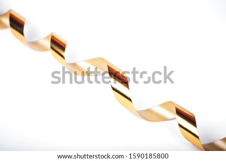 Christmas gold serpentine curling ribbon hanging on white background. Isolated.