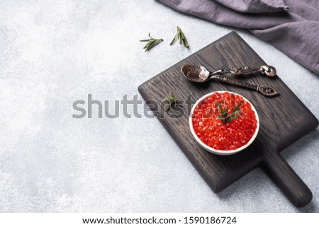 Red salmon caviar in a plate on a wooden cutting Board. Gray concrete background with Copy space. Snack delicacy