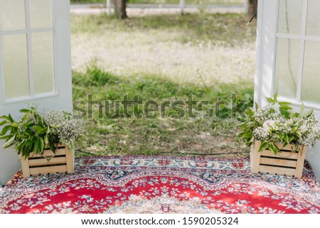 Flowers Bouquet in Wooden Boxes on Vintage Carpet near Doors with Windows Photo. Beautiful Aromatic Composition. Ornamented Floral Plants in Sunny Day. Blurred Green Grass on Background