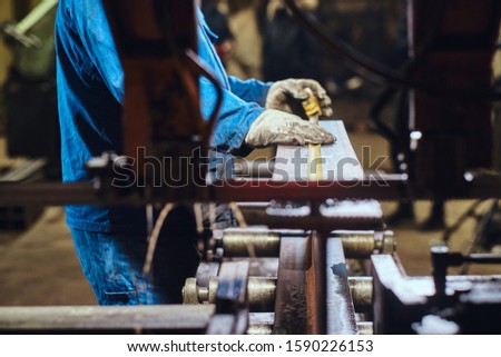 Worker of metal factory is taking a measurements of the piece of rail.