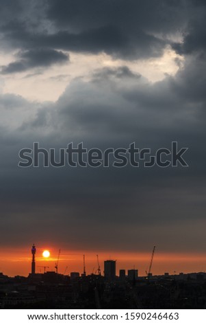A vertical picture of a city silhouette during a beautiful sunset under a cloudy sky