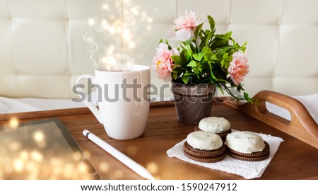 Wooden table, tray, white cup of coffee, flowers on the table, tablet. Sunlight, ray. Abstract bokeh light.
