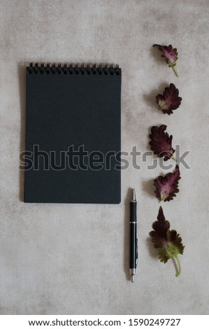 Opened notebook with blank black paper and a pen in grey paper background with frame of red leaves