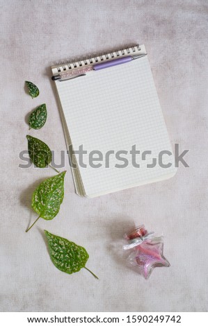 Opened notebook with blank paper and a pen in grey paper background with frame of green and pink leaves