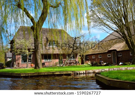 landscape and view of Giethoorn village in Netherlands (Holland) near Amsterdam, canal boat trip and old typical and traditional vintage thatched houses (cottage), famous attraction, destination.  Royalty-Free Stock Photo #1590267727