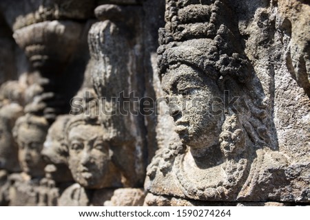 Faces carved in stone at the Borobudur temple on Java, Indonesia. The focus is on the first face and sharpness is fading out in the background.