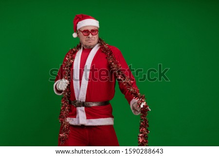 Santa Claus in large pink glasses and with a red garland of tinsel in his hands dancing and posing on a green chrome background