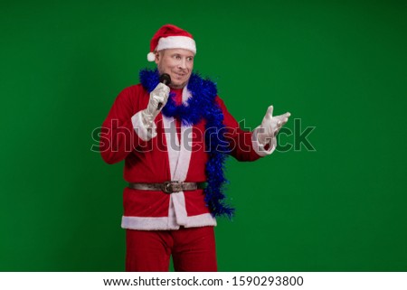 Emotional Santa Claus and a blue garland of tinsel holds a microphone in his hands, sings and gestures on a green chrome background