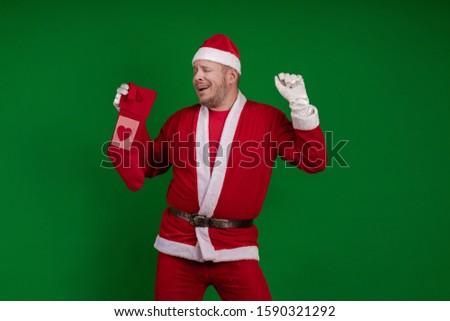 Emotional Santa Claus holds a Christmas sock for gifts in his hands and poses on a green chrome background